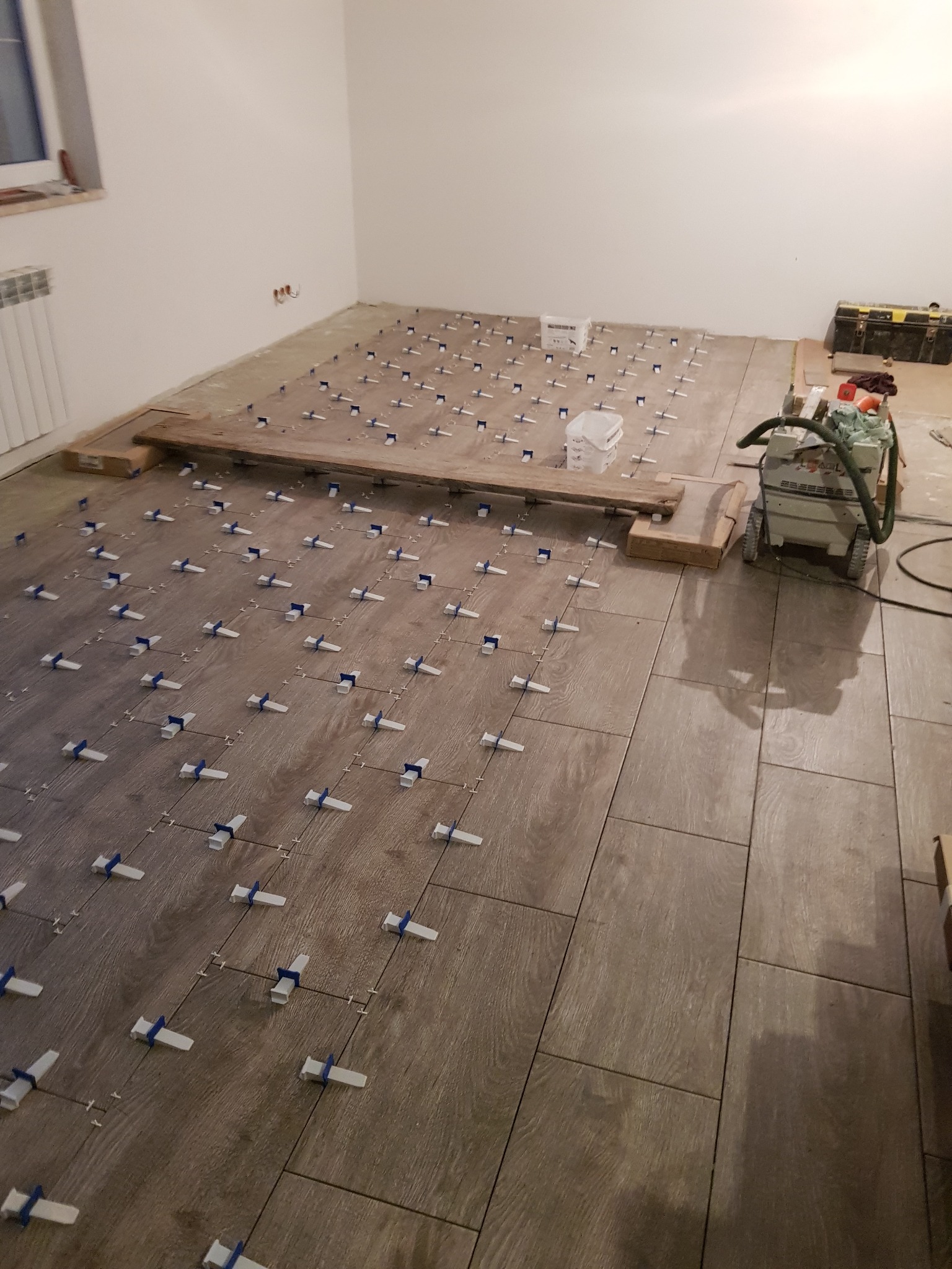 Układanie płytek imitujących drewno z użyciem systemu poziomowania; widoczna maszyna do czyszczenia fug i skrzynka narzędziowa.