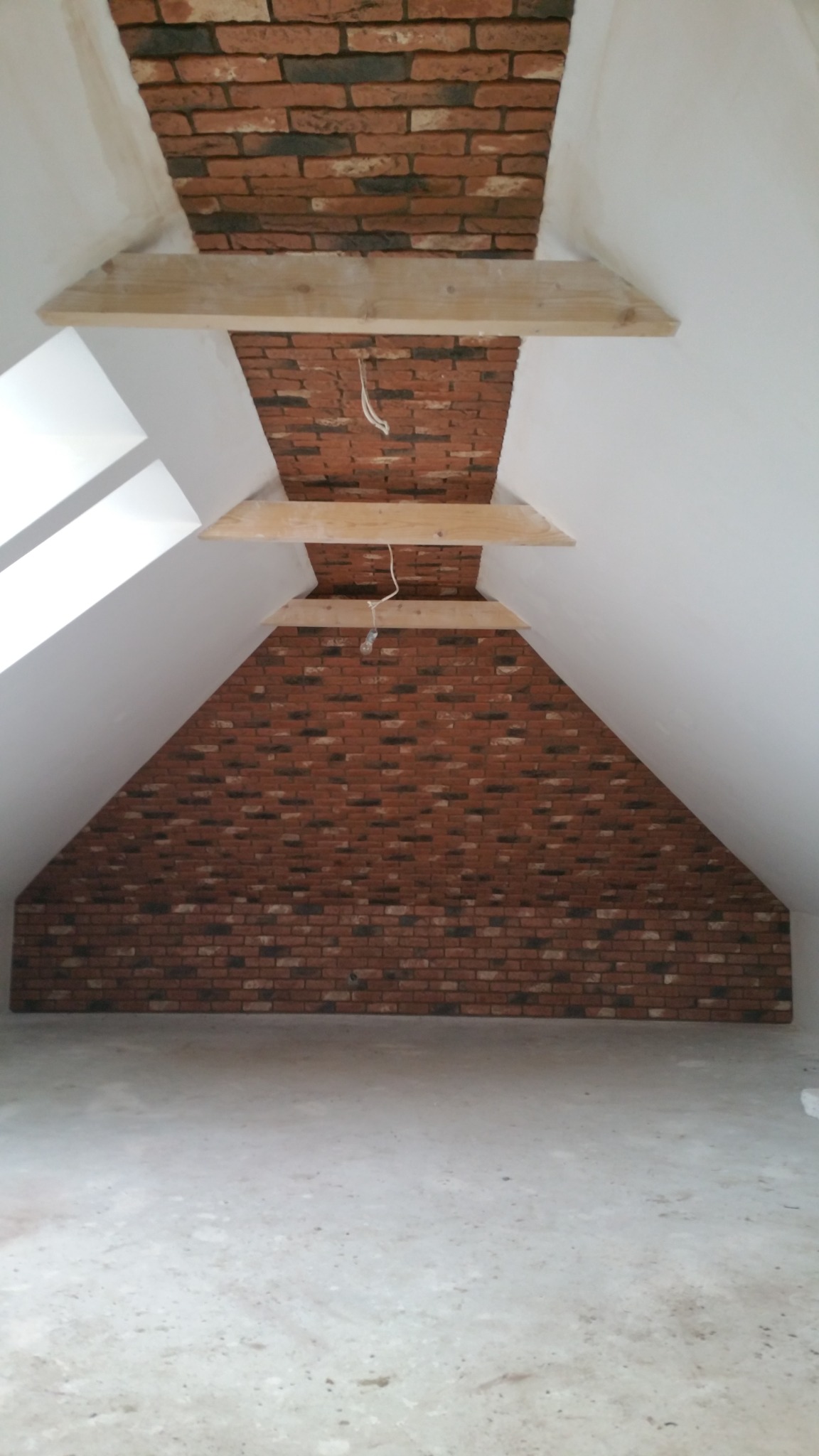 Poddasze po remoncie z fragmentami ściany i sufitu wykończonymi czerwoną cegłą klinkierową, wzmocnione drewnianymi belkami, widoczne kable elektryczne.