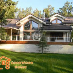 Jasny dom z drewna i cegły z balkonem, otoczony zielenią. Widoczne duże okna i brązowy dach. Na trawniku logo firmy.