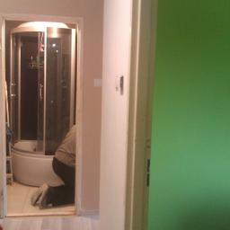 Fin end - Instalacja kabiny prysznicowej w łazience. Widoczna osoba na kolanach, kabina z hydromasażem i fragment zielonej ściany w tle.