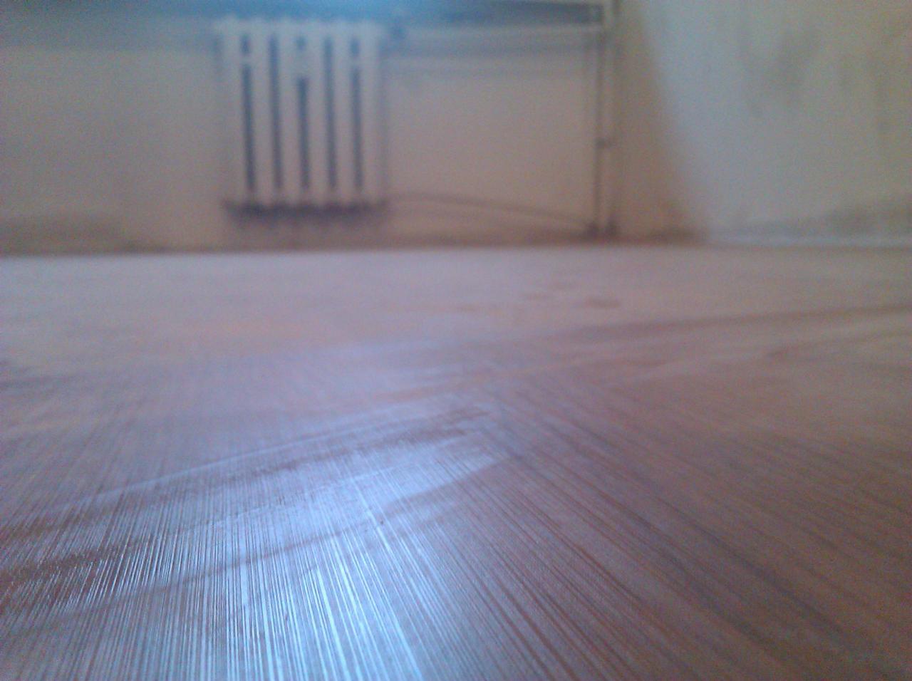 Ukończona drewniana podłoga w pokoju z białym grzejnikiem na ścianie. Widok z niskiej perspektywy ukazuje detale wykończenia.