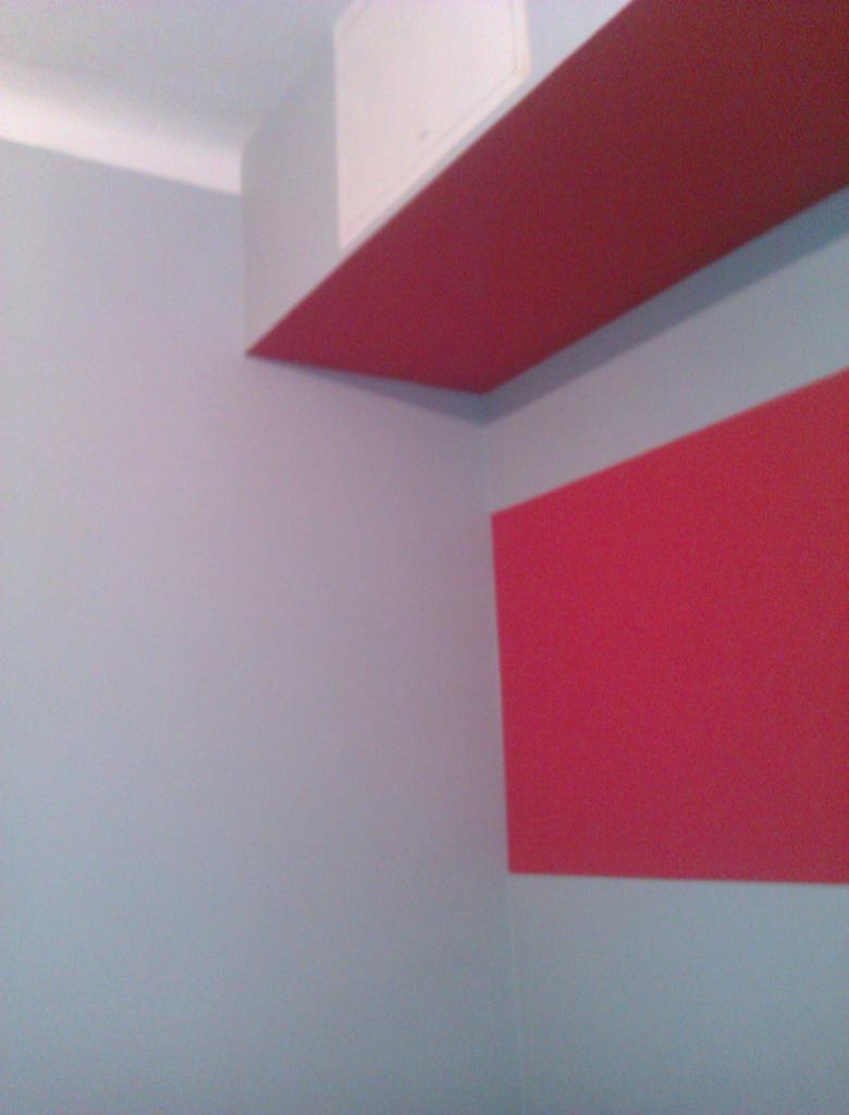 Pomysłowe malowanie ścian w odcieniach szarości i czerwieni, z zabudową nad ścianą. Nietypowe połączenie kolorów i faktur w nowoczesnym wnętrzu.