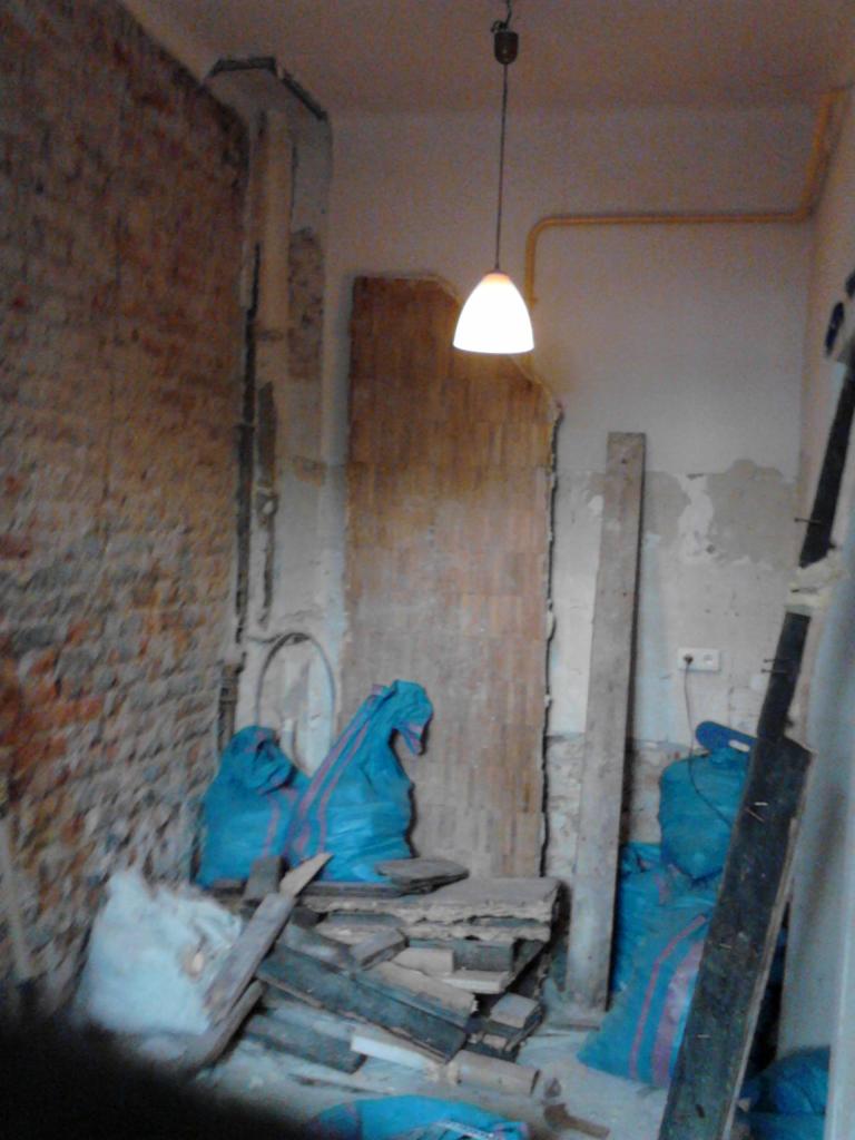 Wnętrze w trakcie demontażu w Lublinie. Odsłonięta cegła, worki z gruzem i wisząca lampa. Przygotowania do remontu.