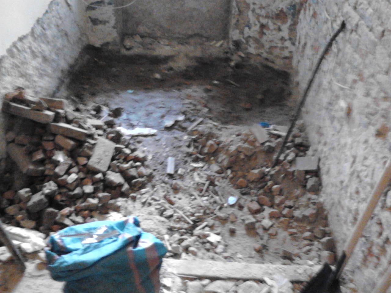 Wnętrze pomieszczenia w trakcie demontażu: gruz, cegły i narzędzia budowlane. Widoczne ślady po skuciu tynku na ścianach z cegły.