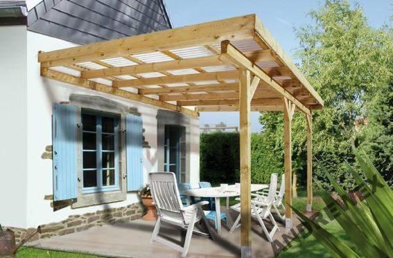 Drewniana pergola z przezroczystym zadaszeniem, przylegająca do białego domu z błękitnymi okiennicami. Na tarasie białe meble ogrodowe.