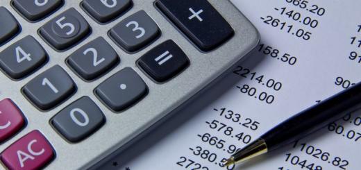 Kalkulator z długopisem na arkuszu kalkulacyjnym z danymi finansowymi. Widoczne liczby i symbole matematyczne. Delikatne oświetlenie.