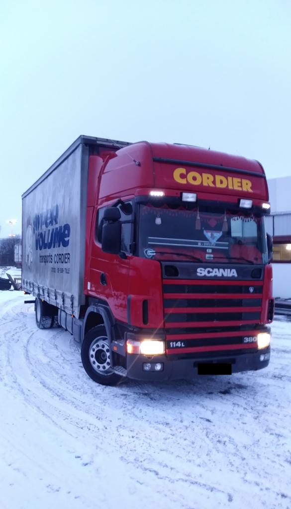 Czerwona ciężarówka Scania 114L 380 z napisem 'Cordier' na tle zimowego krajobrazu, częściowo ośnieżona, z widocznym napisem 'Hyper Volume Transports Cordier' na boku naczepy.
