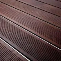 Ciemnobrązowa deska tarasowa z wyraźnym ryflowaniem, ułożona pod kątem, z widocznymi szczelinami, tworząca regularny wzór.