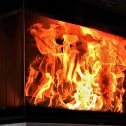 SPARTAKUS-BAU SEBASTIAN ZYZAŃSKI - Płomienie wewnątrz kominka z szybą, widoczne detale konstrukcji i faktura kamiennej obudowy.