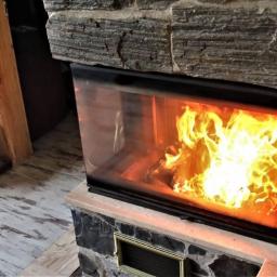 SPARTAKUS-BAU SEBASTIAN ZYZAŃSKI - Zamknięty kominek z płonącym ogniem, obudowany kamieniem w odcieniach szarości, z widoczną dekoracyjną figurką obok.