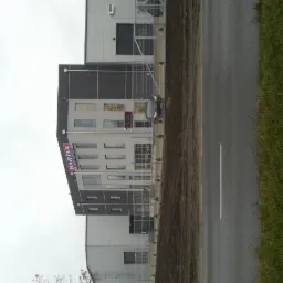 Szary budynek biurowy z logo Bartex Wine & Spirits, widoczny z ulicy w pochmurny dzień. Metalowe ogrodzenie i trawa w tle.