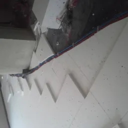 Białe płyty styropianowe układane na podłodze, z widocznymi przewodami instalacji. Przygotowanie do ogrzewania podłogowego z przewodami w kolorze niebieskim i czerwonym.