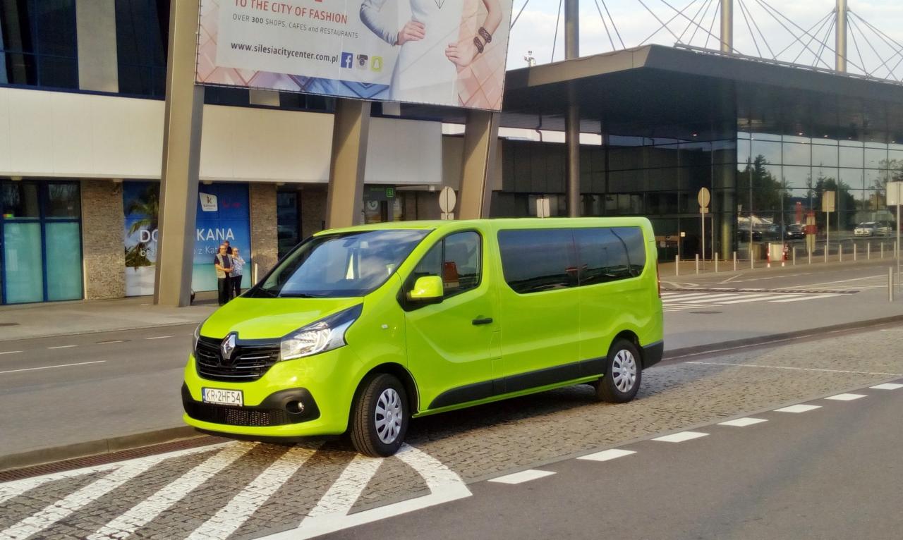 Jasnozielony bus Renault Trafic z polskimi tablicami rejestracyjnymi KR-2HF54 zaparkowany przed budynkiem Silesia City Center na tle plakatu reklamowego.