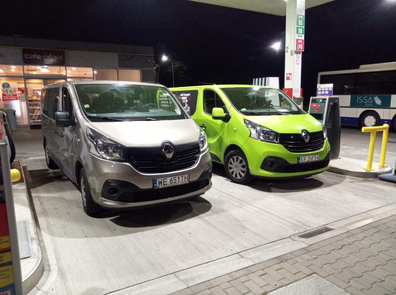 Dwa busy Renault Trafic: beżowy z rejestracją WE 651TH i limonkowy z rejestracją KR 2HF54, stojące na stacji benzynowej nocą, z widocznym punktem Cafe Punkt i autobusem Issa Tour w tle.