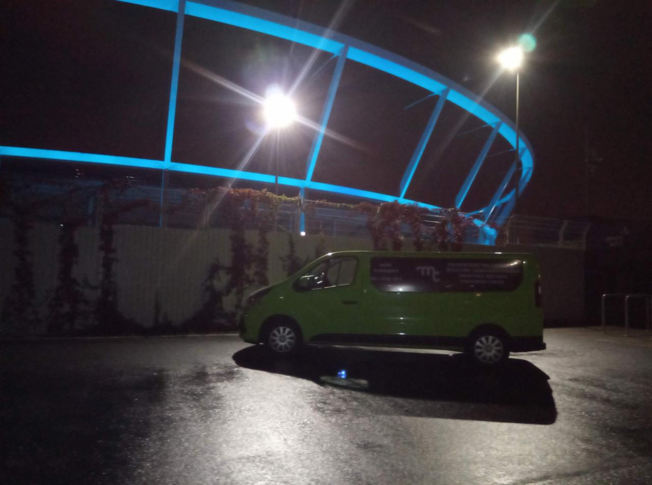 Zielony van z reklamą firmy zaparkowany nocą pod oświetlonym na niebiesko wiaduktem.