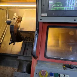 Wnętrze maszyny CNC z widocznym uchwytem narzędziowym, elementami sterującymi i wyświetlaczem parametrów pracy. Na panelu sterowania leżą suwmiarki.