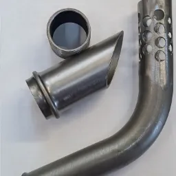 Surowe elementy metalowe: pierścień, stożkowa rura i wygięta rura z otworami, leżące na białym tle.