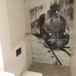 Nowoczesna łazienka w Gogołowie z toaletą podwieszaną i kabiną prysznicową typu walk-in, wyróżniająca się ścianą z grafiką lokomotywy parowej w stylu retro.