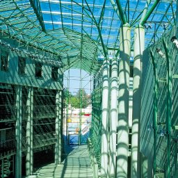 Moryc Studio - Wnętrze budynku z przeszklonym dachem i zieloną konstrukcją nośną. Widoczne kolumny i gra świateł. Architektura industrialna z elementami nowoczesności.