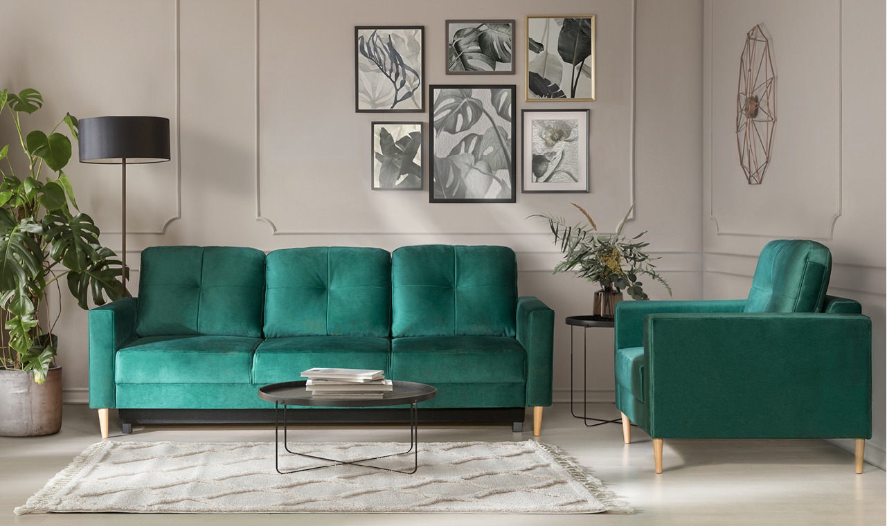 Aranżacja wnętrza: szmaragdowa sofa i fotel na tle ściany z galerią obrazów botanicznych. Całość doświetlona lampą podłogową, z rośliną doniczkową po lewej.