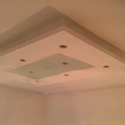 Sufit podwieszany z płyt gipsowych w trakcie montażu, widoczne otwory na oświetlenie i fragmenty szpachlowania, surowe ściany w tle.