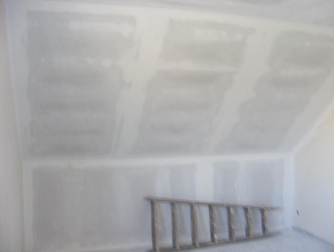 Pokój po szpachlowaniu, widoczna drabina oparta o ścianę. Ściany i skośny sufit pokryte szpachlą, przygotowane do dalszych prac wykończeniowych.