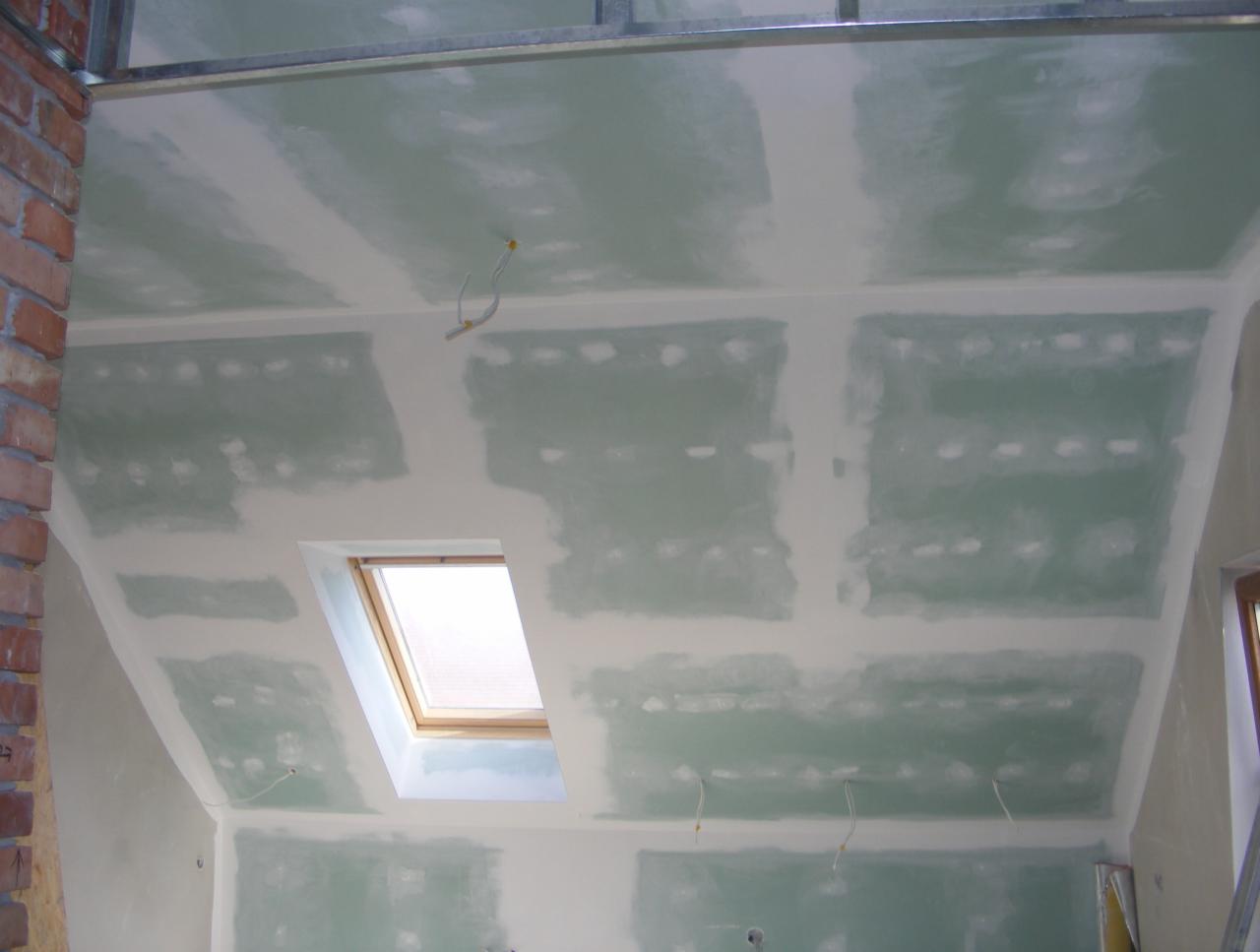 Sufit poddasza ze skosem i oknem dachowym po szpachlowaniu, widoczne płyty gipsowo-kartonowe i metalowa konstrukcja nośna.