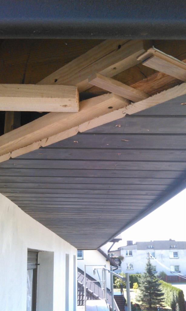 Montaż drewnianej podbitki dachowej na balkonie. Widoczne deski konstrukcyjne i elementy wykończeniowe. Ujęcie od dołu.