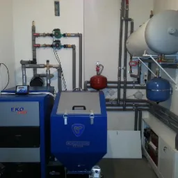 Kompleksowa kotłownia z piecem EKO Plus i Ognivo Biecz, zbiornikami wyrównawczymi i rozbudowaną instalacją hydrauliczną w pomieszczeniu technicznym.
