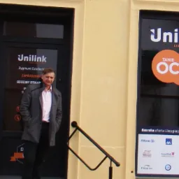 Przedstawiciel Unilink stoi przed biurem z reklamą tanich ubezpieczeń OC i AC, widoczne logo firm ubezpieczeniowych.