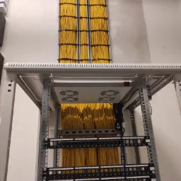 Profesjonalnie ułożone żółte kable sieciowe w szafie rack, widoczne panele krosownicze z numeracją portów, wentylatory chłodzące i elementy mocujące.