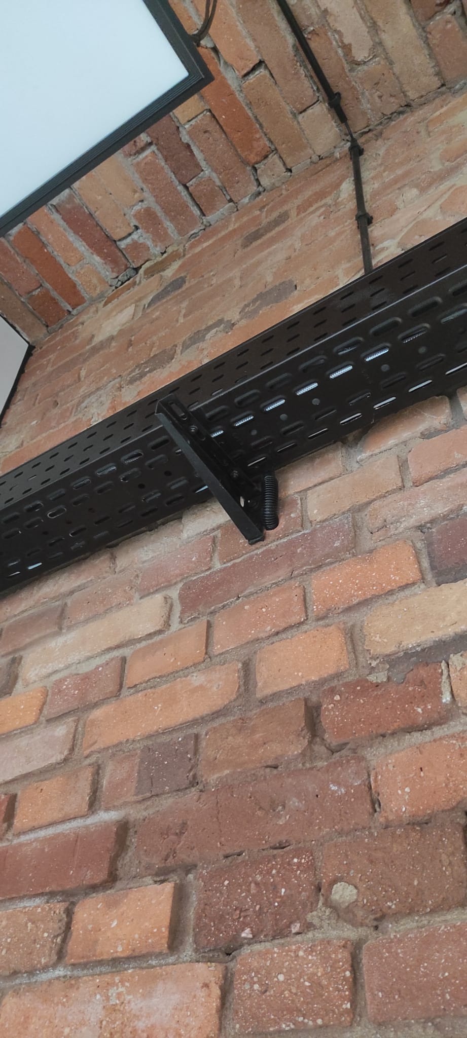 Czarna korytka kablowa zamontowana na ceglanej ścianie w Jeleniej Górze, widoczne mocowanie i peszel. Instalacja poprowadzona wzdłuż ściany.