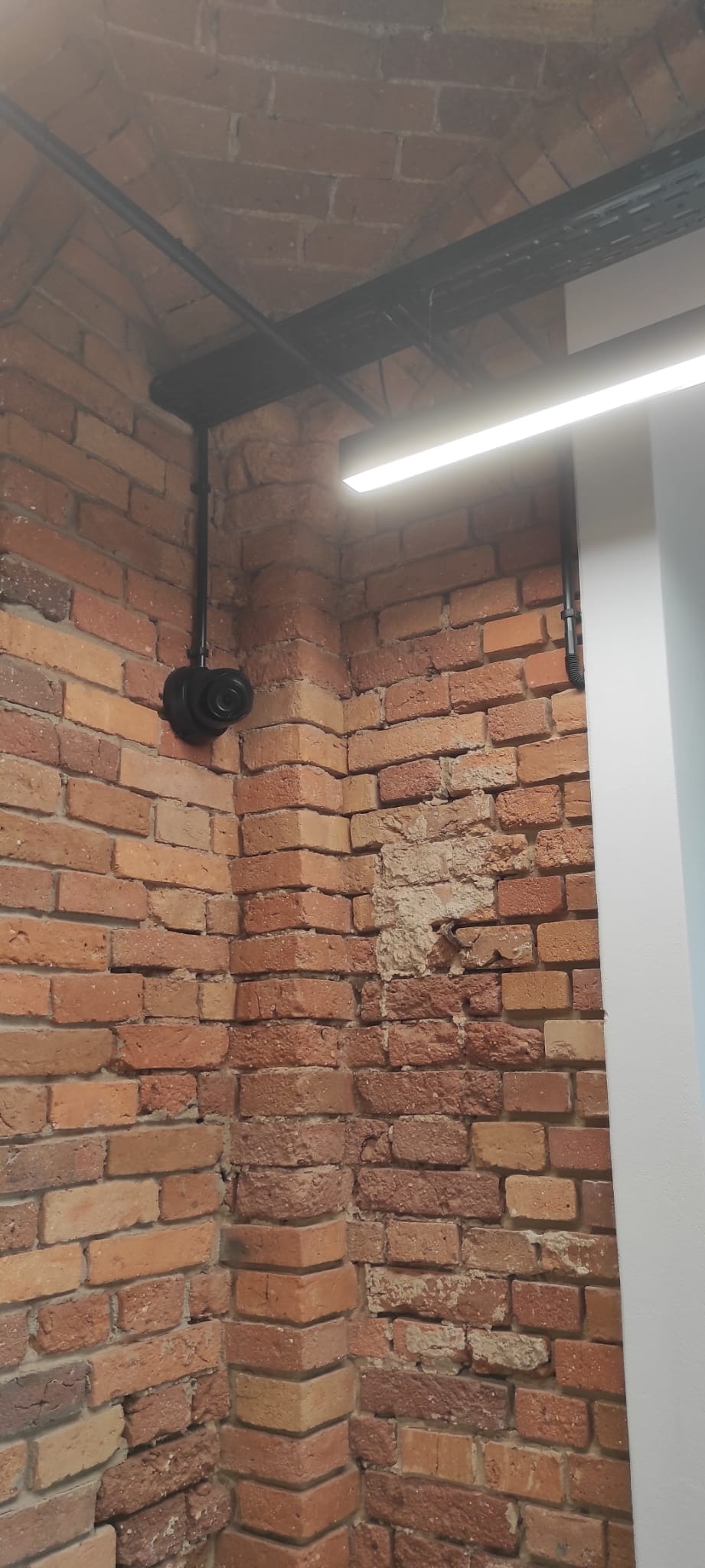 Kamera monitoringu zamontowana na ceglanej ścianie, widoczne kable i oświetlenie ledowe.