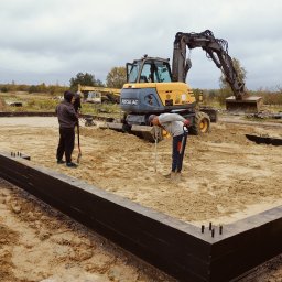 P.H.U Emilka Emilia Wołczyńska - Przygotowanie terenu pod fundamenty domu jednorodzinnego z użyciem mini koparki Mecalac i niwelatora laserowego, widoczne drewniane szalunki pomalowane na czarno i wystające pręty zbrojeniowe.