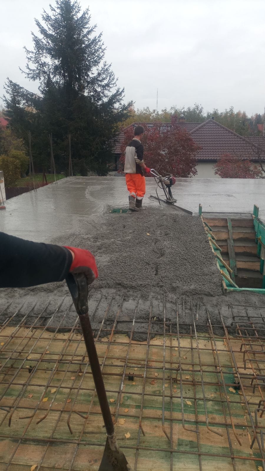 Wylewanie betonu na strop budynku, widoczny pracownik zacierający powierzchnię betonu za pomocą wibratora, w tle zabudowa jednorodzinna
