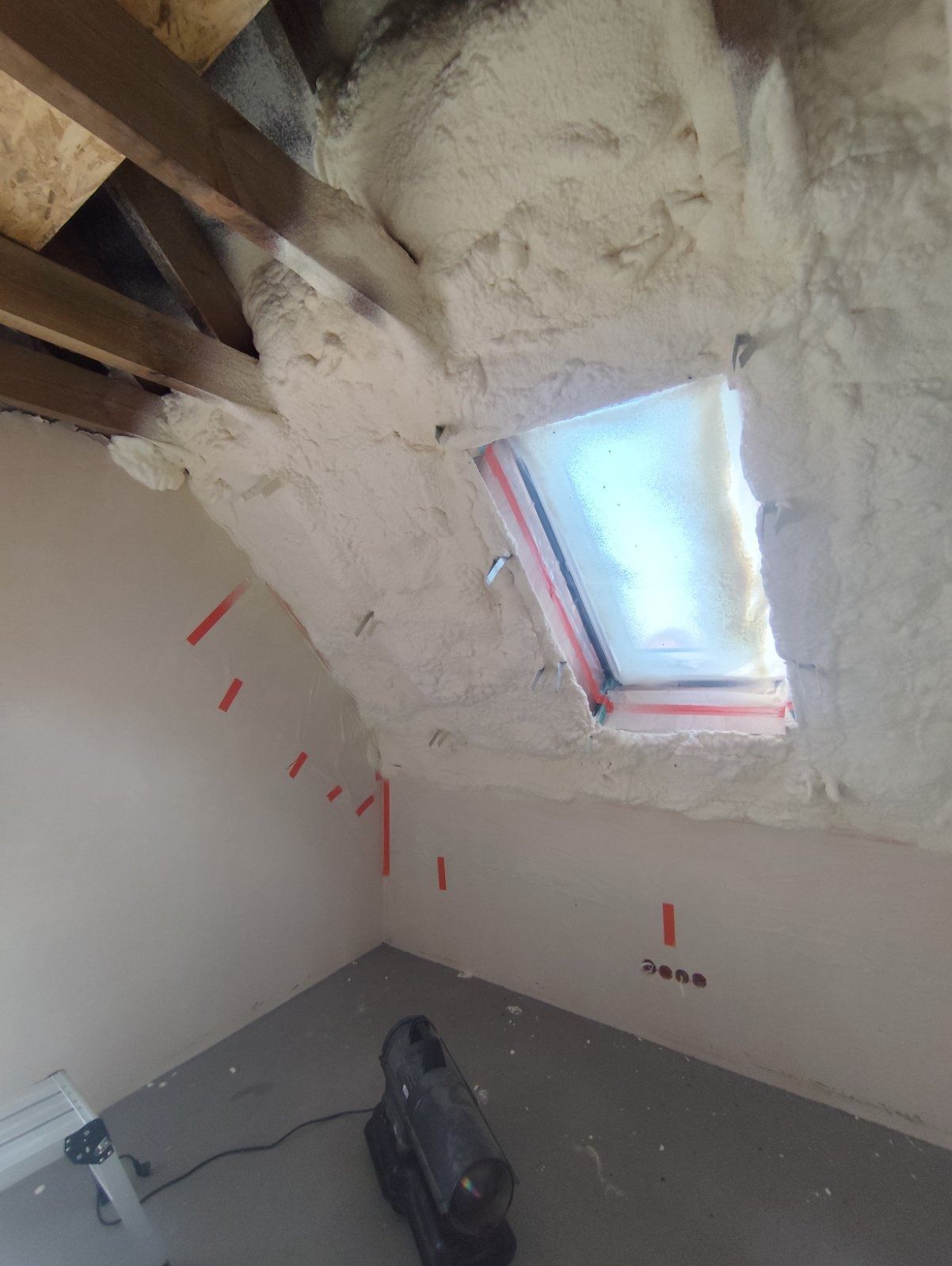 Poddasze po ociepleniu pianką PUR, widoczne krokwie, okno dachowe i ściany z taśmami zabezpieczającymi.