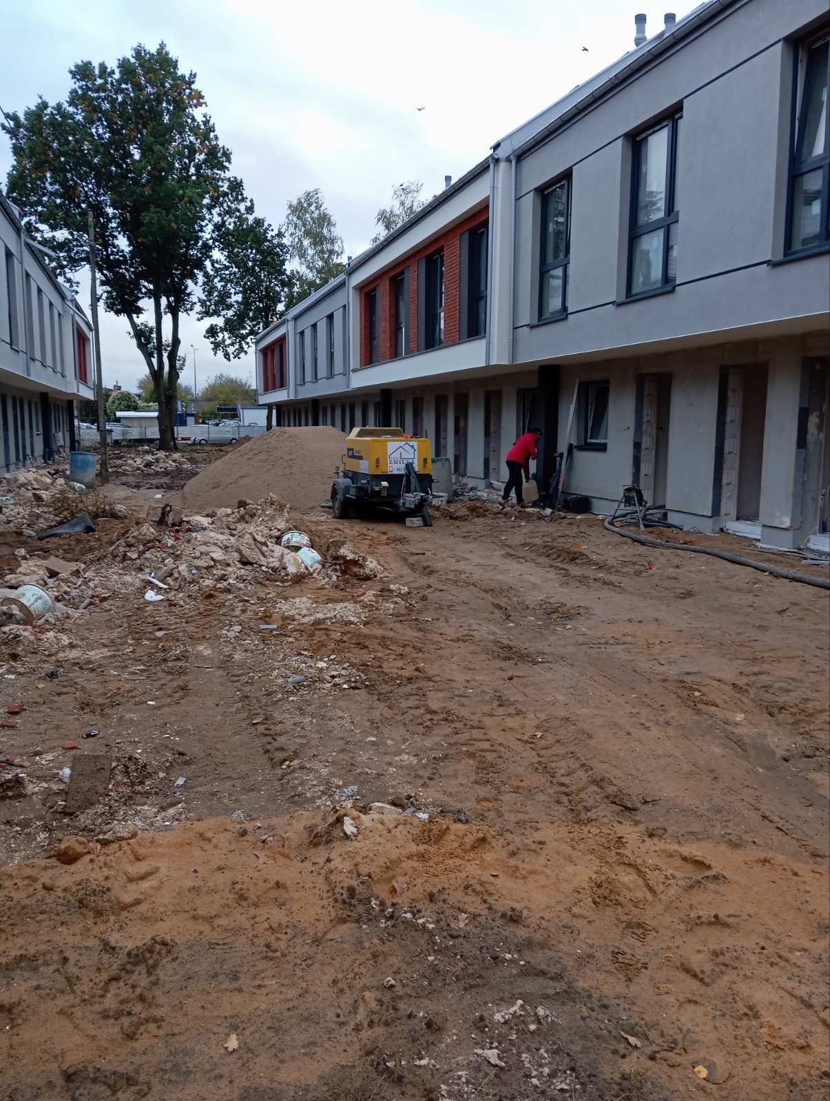 Budowa szeregowców w Kampinosie: teren przygotowany pod wylewkę, widoczny agregat do podawania betonu i pracownik w czerwonej kurtce.