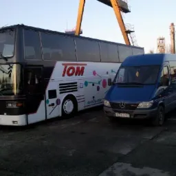 Czarno-biały autobus piętrowy TOM i niebieski bus Mercedes na tle żurawia portowego. Usługi transportowe.