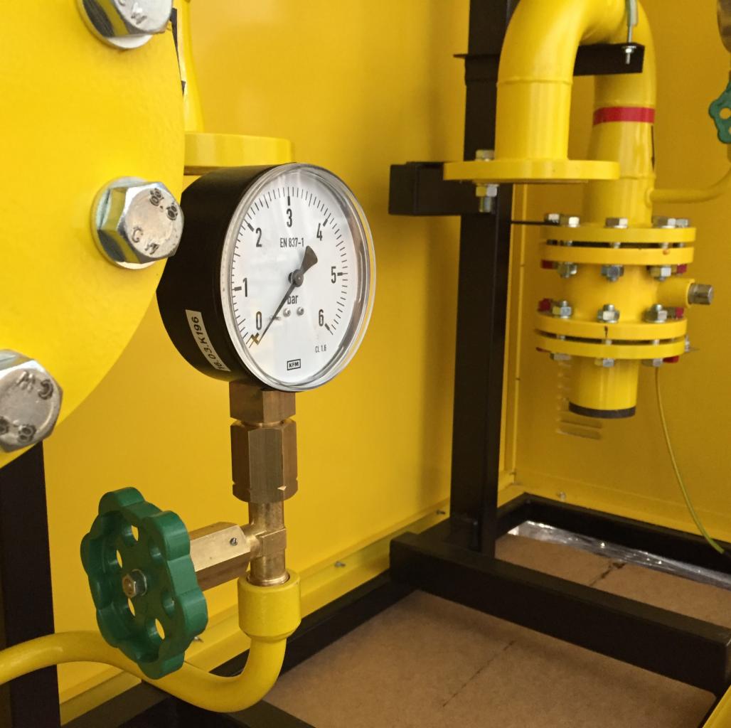 Żółta instalacja gazowa z manometrem i zaworem z zielonym pokrętłem w obudowie na czarnej ramie.