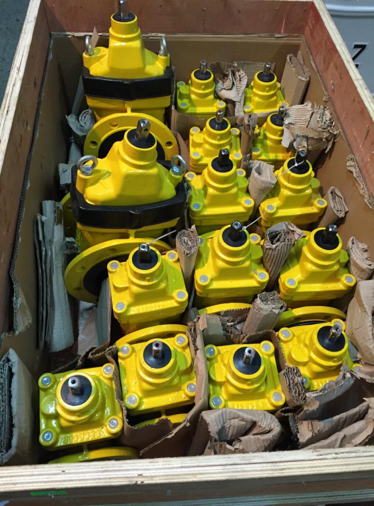 Żółte zawory regulacyjne z kołnierzami i bez, umieszczone w drewnianej skrzyni transportowej z tekturowymi przekładkami.