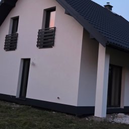 PIK-EL USŁUGI BUDOWLANE DAWID PIKUL - Biały dom jednorodzinny z ciemną dachówką i stolarką okienną, świeżo po malowaniu elewacji, widok z boku na tle błękitnego nieba o zmierzchu.