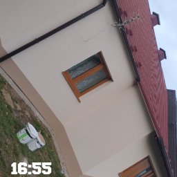 PIK-EL USŁUGI BUDOWLANE DAWID PIKUL - Elewacja domu po malowaniu w dwóch odcieniach beżu, z widocznymi detalami jak okna z drewnianą ramą i brązowe rynny. Na pierwszym planie puszki z farbą.