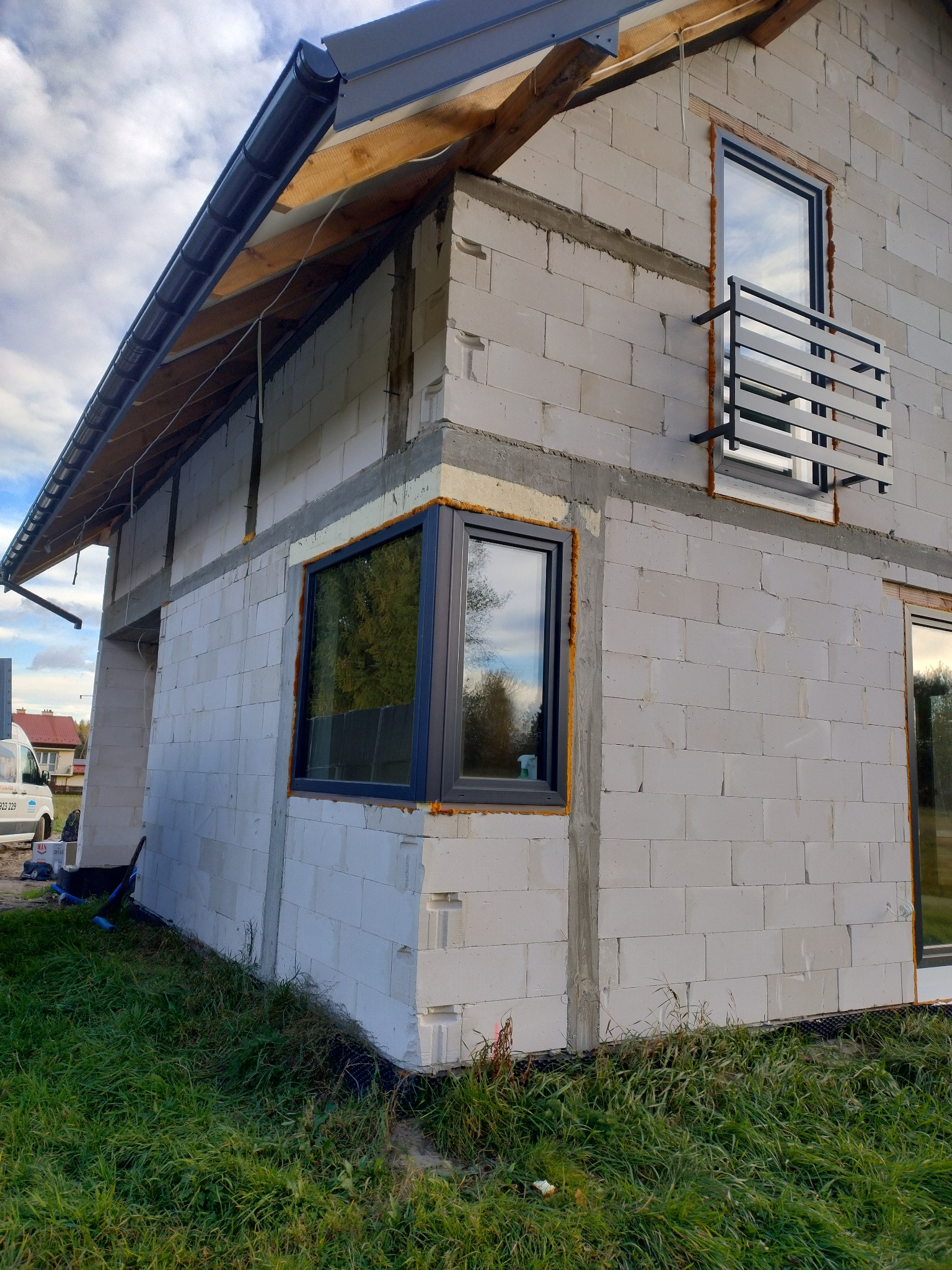 Surowy stan budynku z betonu komórkowego z zamontowanymi oknami i balkonem, widoczne detale łączeń i pianki montażowej, trawa w dole kadru.