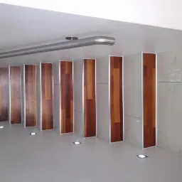 Nowoczesne wykończenie wnętrza z panelami drewnopodobnymi wertykalnie ułożonymi pomiędzy płytkami imitującymi marmur, oświetlenie punktowe w podłodze, widoczna rura pod sufitem.