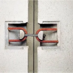 Połączenie dwóch betonowych prefabrykatów za pomocą metalowego łącznika z elementami z czerwonego tworzywa, widoczne wgłębienia w betonie.