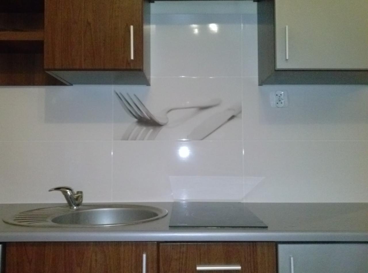 Wykończona kuchnia z białymi płytkami z motywem sztućców nad zlewem i płytą grzewczą. Widoczne szafki wiszące i blat.