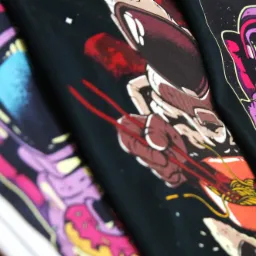 Kolekcja czarnych koszulek z nadrukami kosmonautów jedzących spaghetti, pizzę i pączki, ułożonych obok siebie, prezentujących różne projekty graficzne.