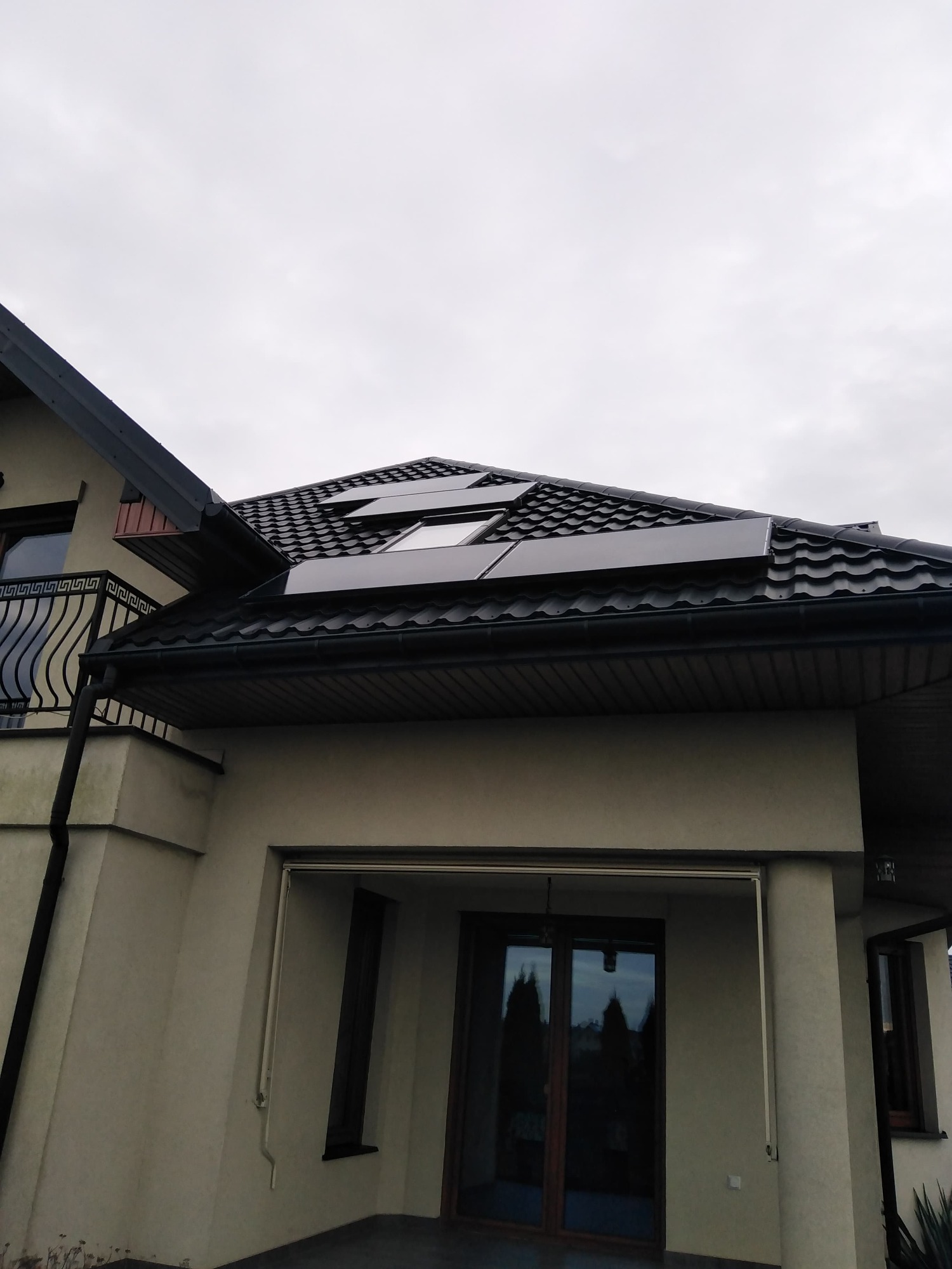 Dom jednorodzinny z panelami słonecznymi na czarnym, metalowym dachu w pochmurny dzień.