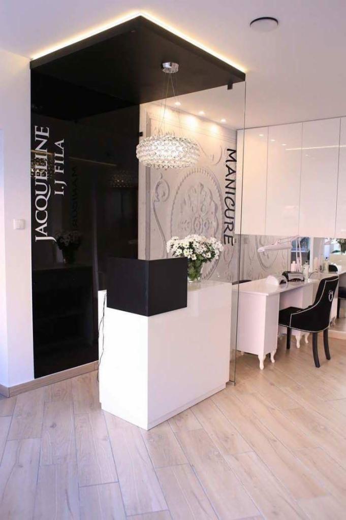 Nowoczesne wnętrze salonu kosmetycznego z recepcją w kolorach bieli i czerni, dekoracyjna lampa wisząca, stanowisko do manicure z czarnym krzesłem.