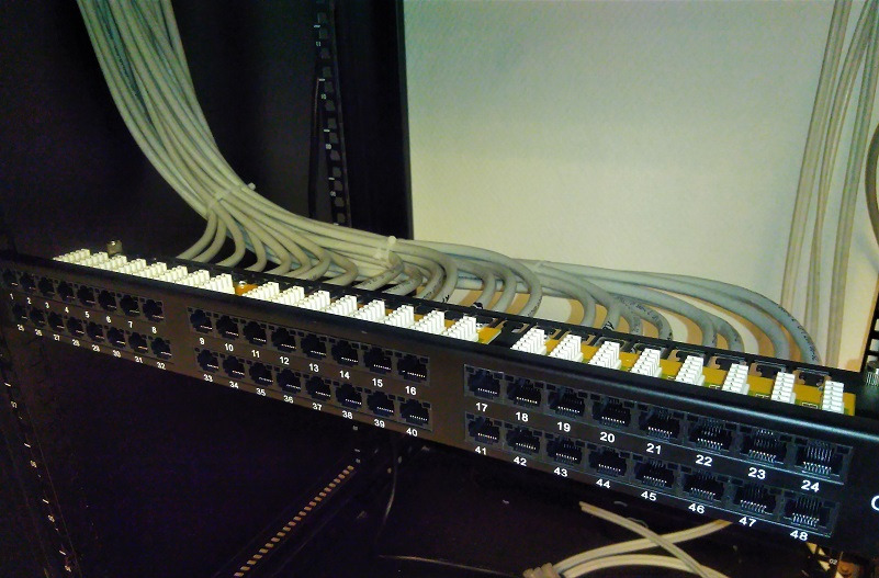 Panel krosowniczy z podłączonymi kablami sieciowymi w szafie rack, widoczne numery portów od 1 do 48.